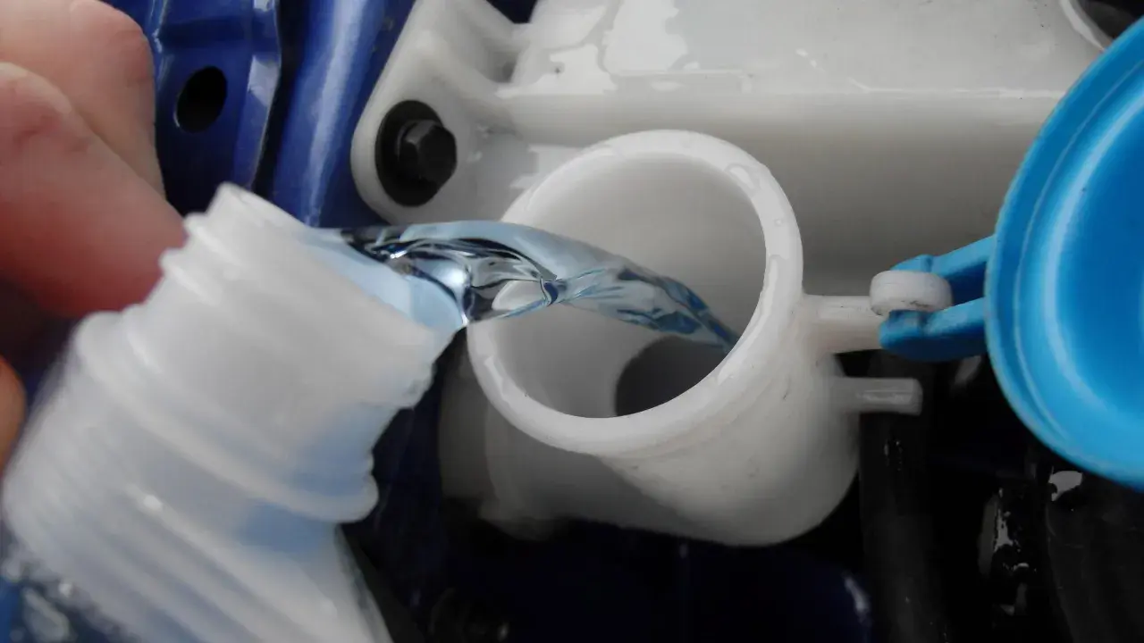 Flüssigkeit wird aus einer Flasche in den Behälter für Scheibenwischwasser gegossen. So einfach kann man Scheibenwischwasser selber machen.