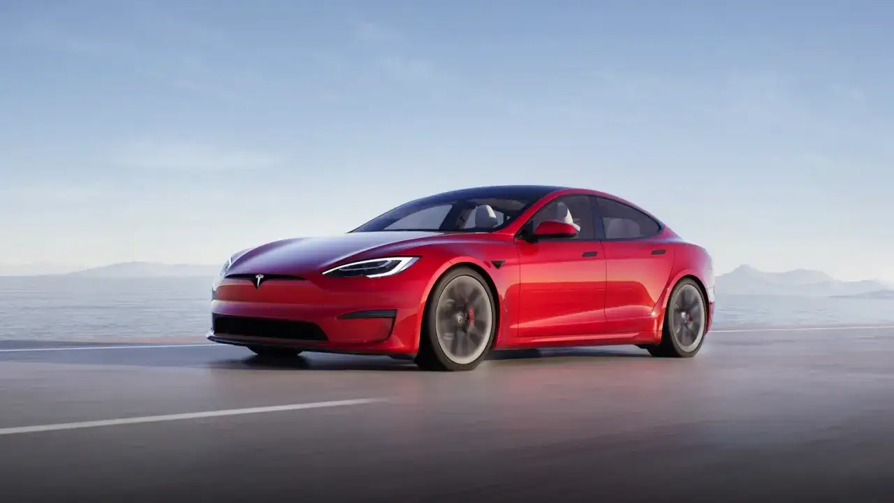Roter Tesla Model S fährt auf einer Straße am Meer entlang.