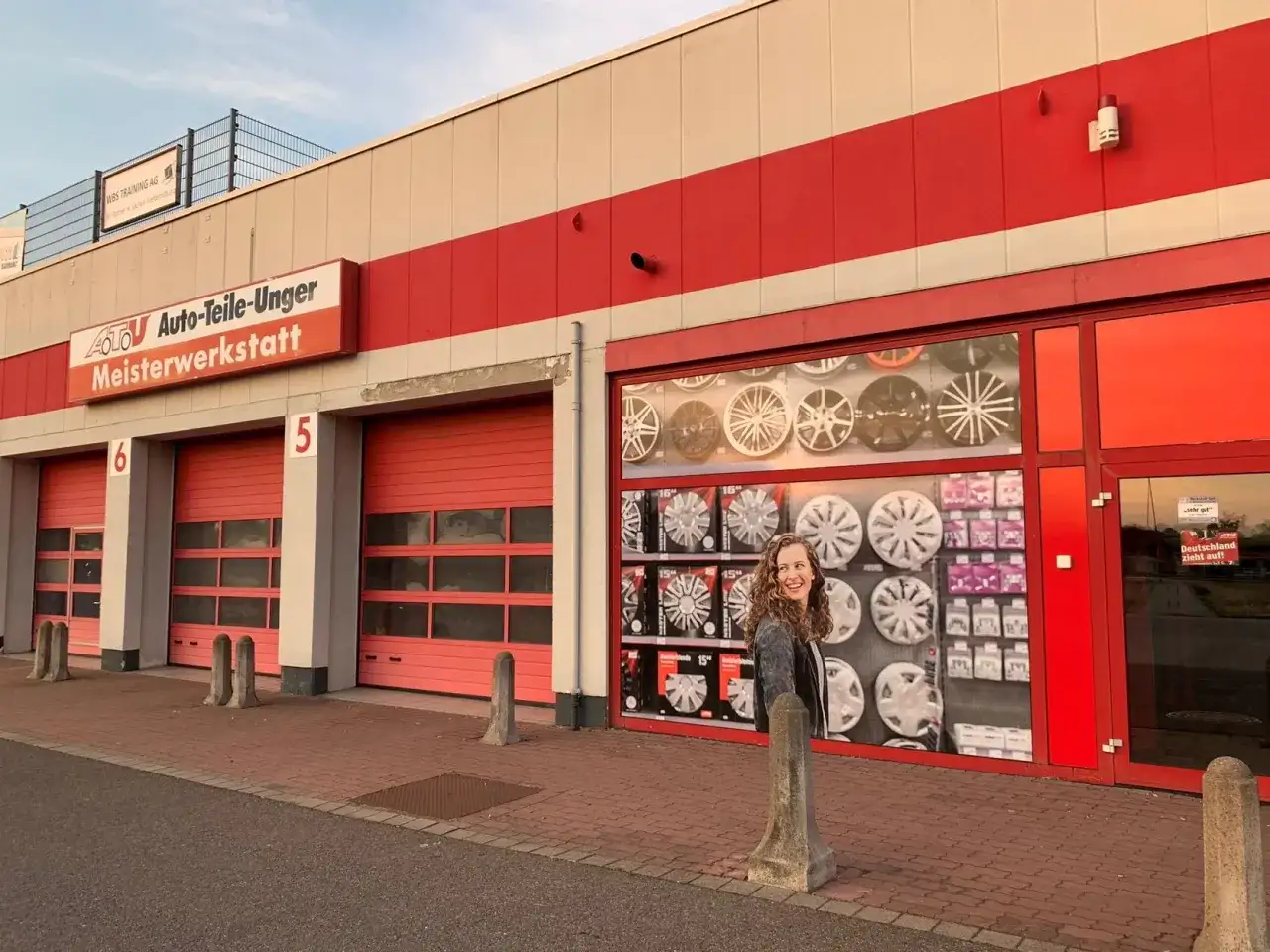 Frau vor ATU Auto-Teile-Unger Meisterwerkstatt in Köln. Viele Felgen und Radkappen im Schaufenster.