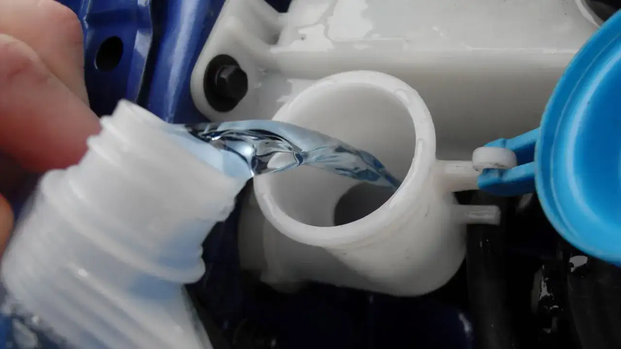 Flüssigkeit wird aus einer Flasche in den Behälter für Scheibenwischwasser gegossen. So einfach kann man Scheibenwischwasser selber machen.