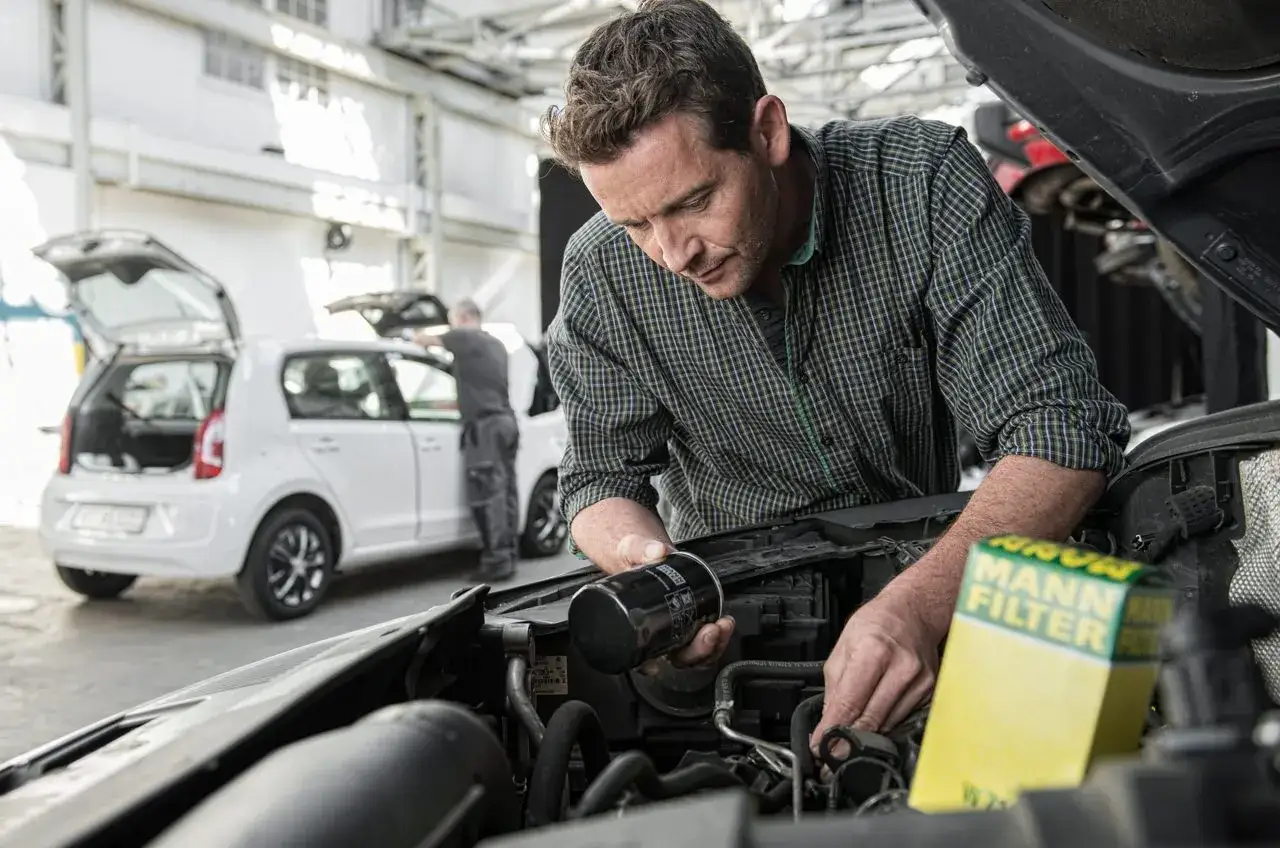 Ein Mann mit einem Ölfilter von Mann-Filter in der Hand, der an einem Auto arbeitet.